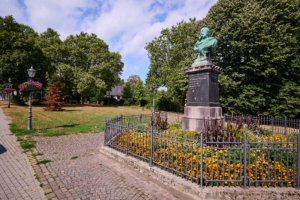 Denkmal am Rellinghauser Markt in Essen-Stadtwald mit Blumenbeet, Laterne und alten Bäumen