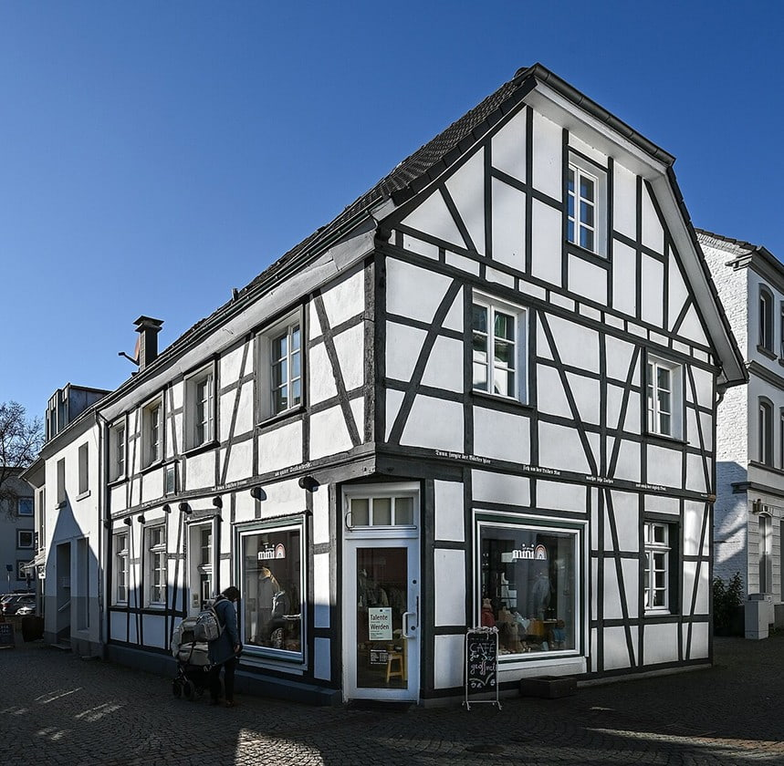Weißes Fachwerkhaus mit dunklen Balken und Ladengeschäft an einer Straßenecke in der Altstadt von Werden.