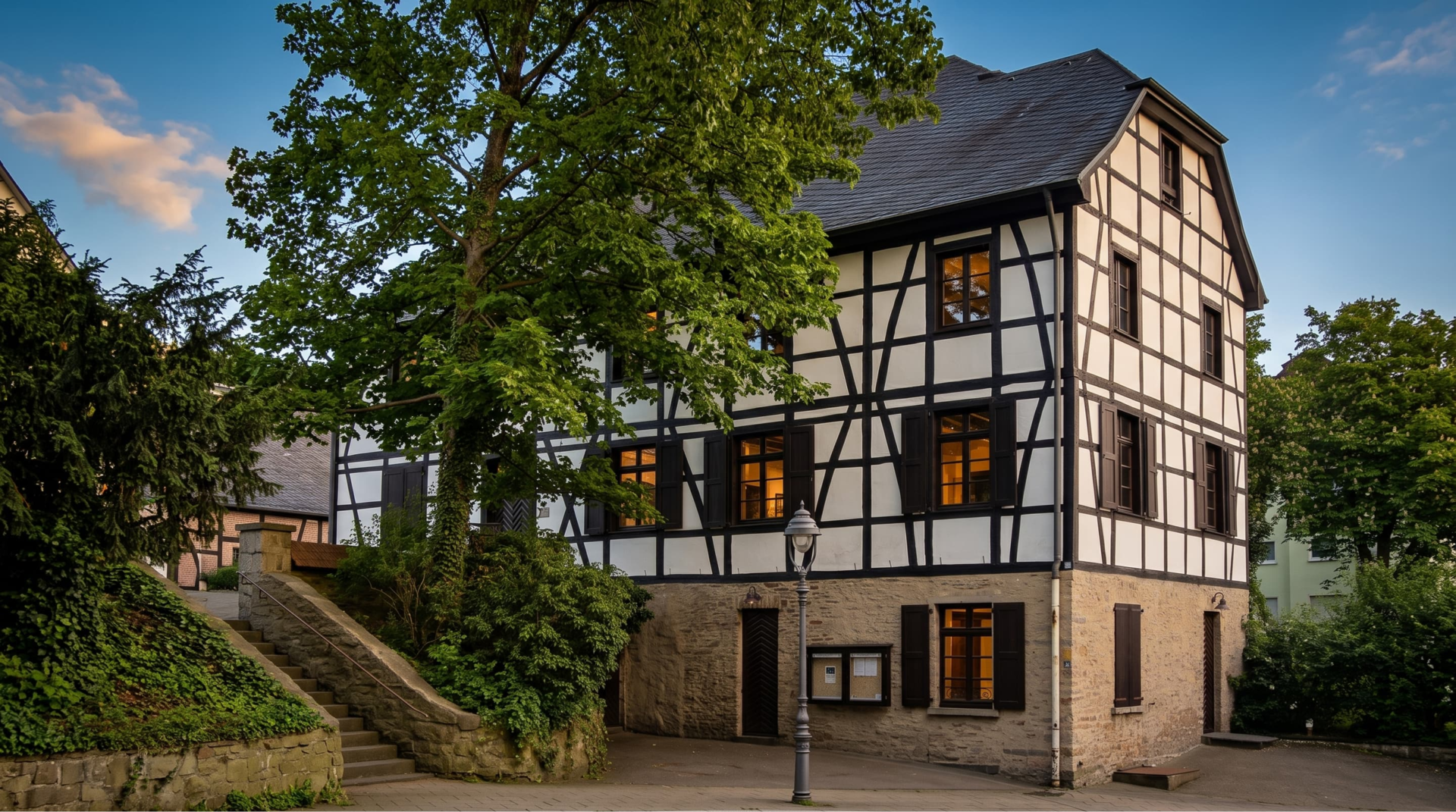 Historisches Fachwerkhaus in Essen-Werden mit steinernem Sockel, Außentreppe und altem Straßenlaternenmast.