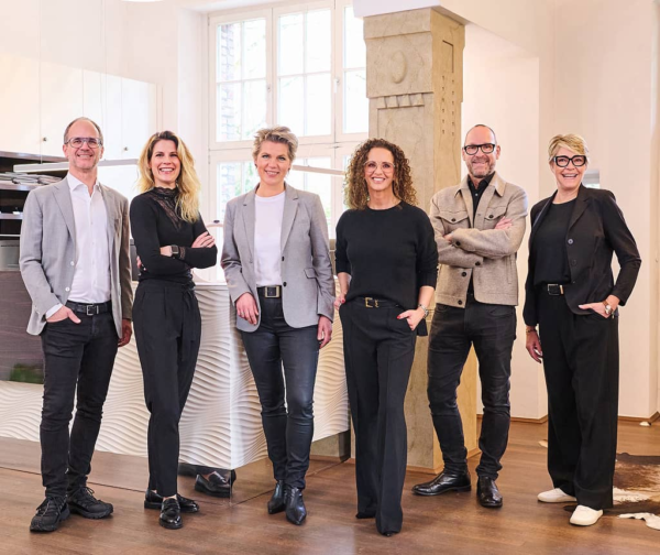 Sechsköpfiges hey-Team steht lächelnd in modernem Showroom