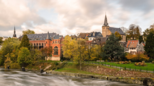 Historische Altstadt mit Kirche, Wohnhäusern und herbstlichen Bäumen am Fluss.