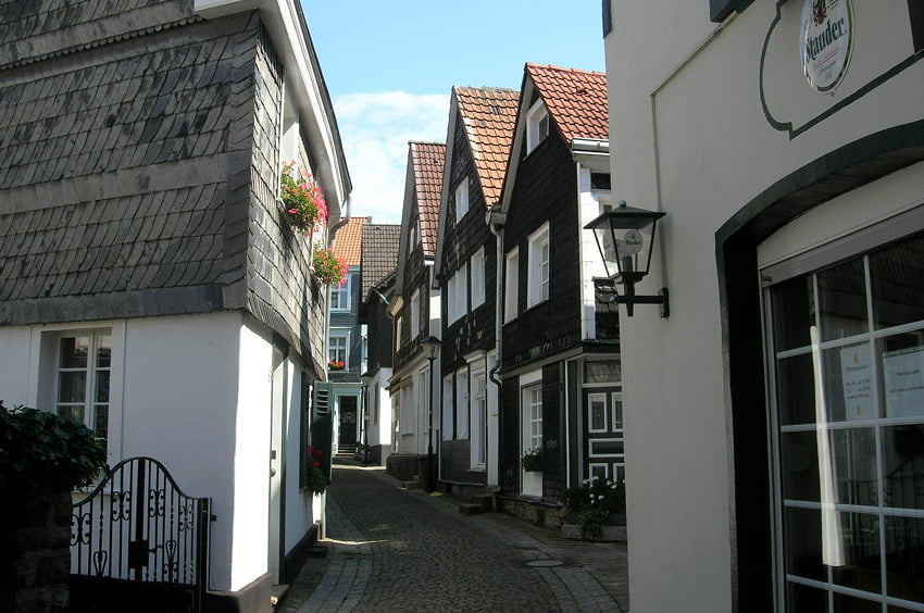 Schmale gepflasterte Gasse mit historischen schieferverkleideten Häusern.
