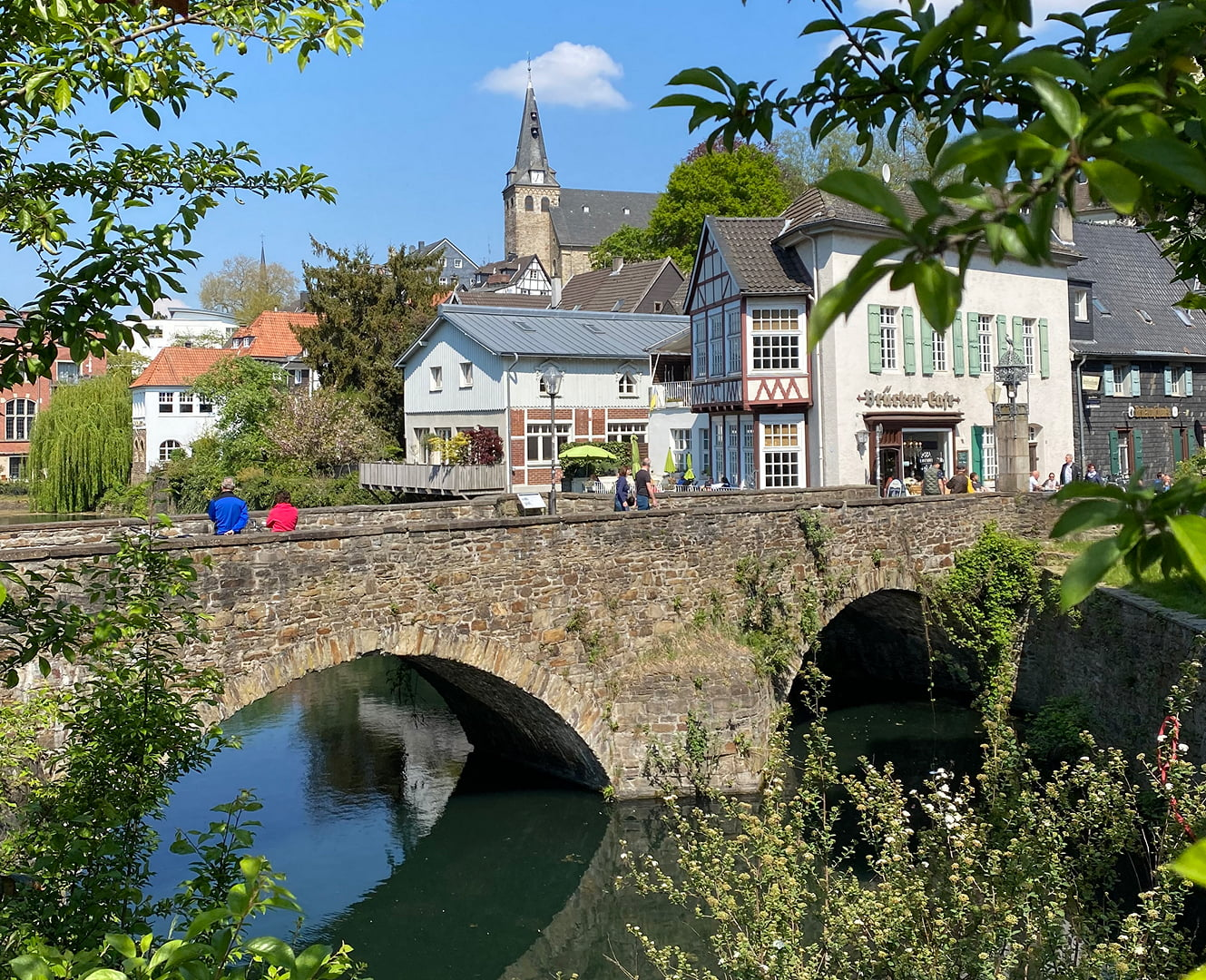 Historische Steinbrücke über einem Fluss mit Altstadtbebauung und Kirche im Hintergrund.
