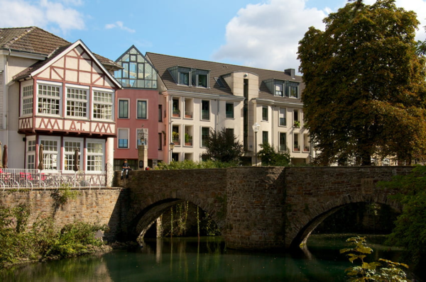 Historische Steinbrücke über einem Gewässer mit Wohnhäusern im Hintergrund.