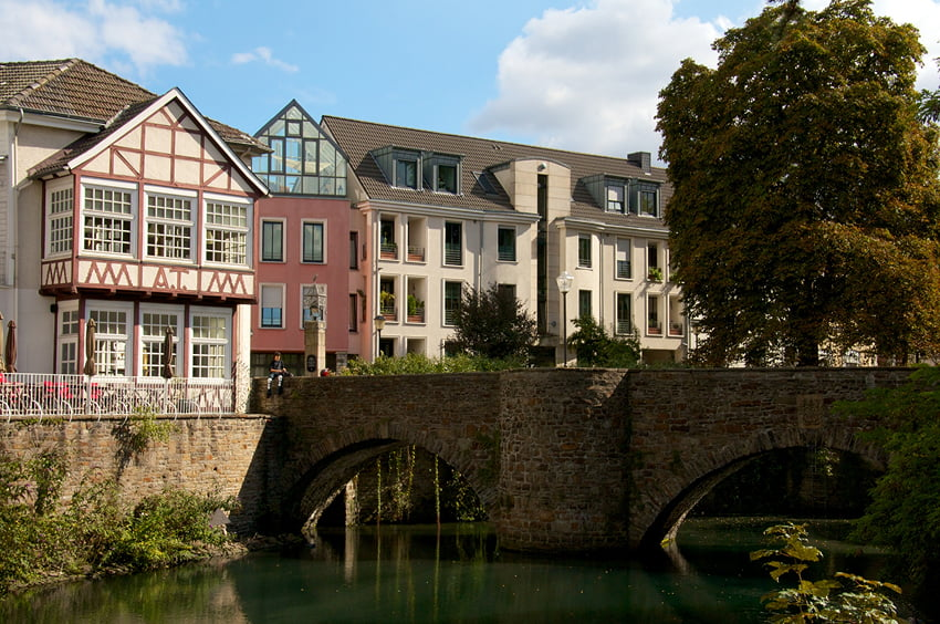 Historische Steinbrücke über einem Gewässer mit Wohnhäusern im Hintergrund.