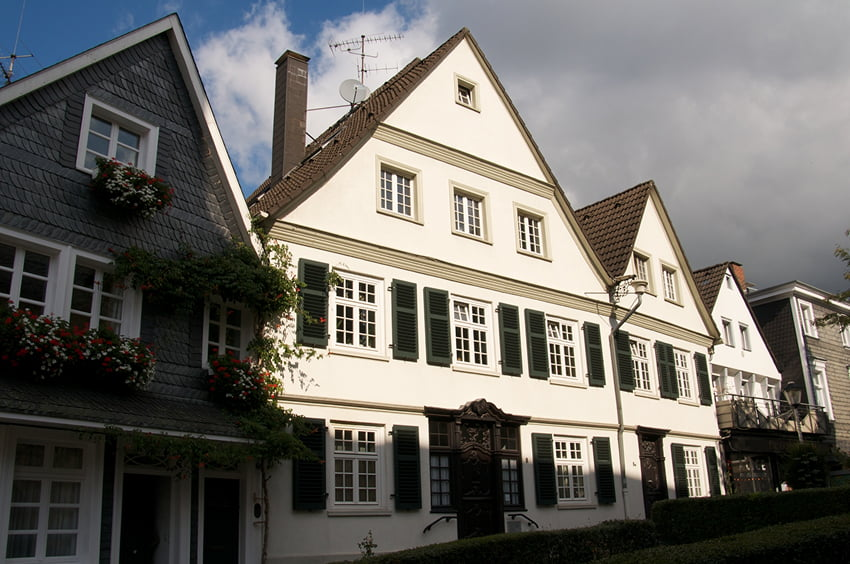 Historische Wohnhäuser mit hellen Fassaden, grünen Fensterläden und Satteldächern.