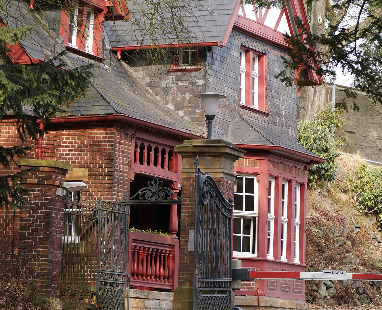 Historisches Gebäude mit roter Backsteinfassade, grauem Schieferdach und schmiedeeisernem Eingangstor.