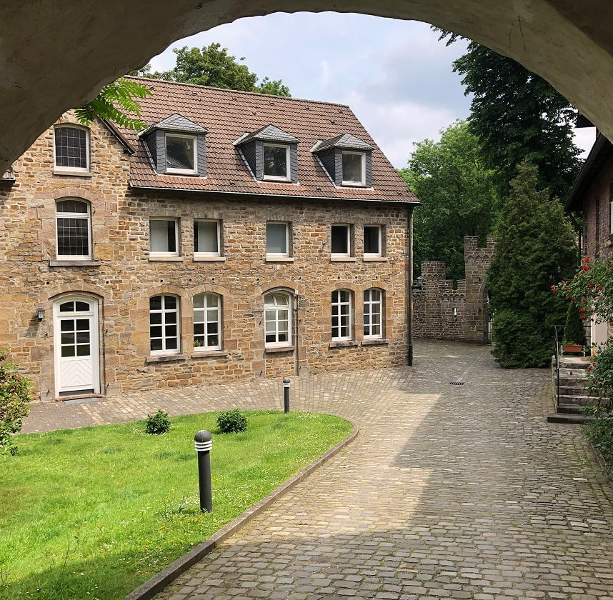 Historisches Steinhaus mit gepflastertem Innenhof und begrünter Umgebung.
