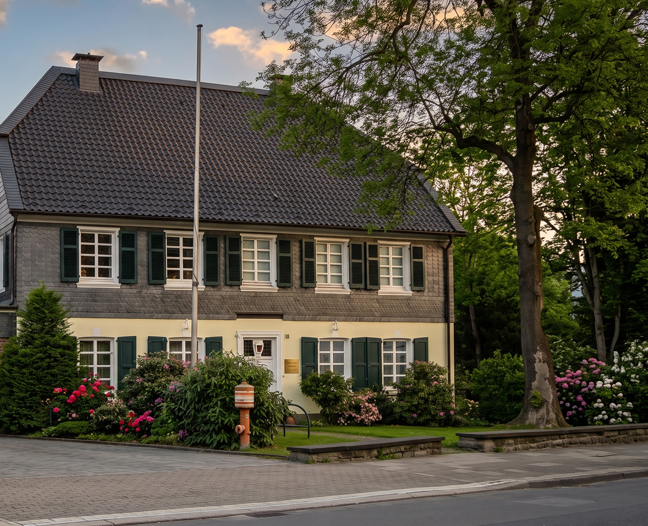 Historisches Wohnhaus mit Schieferfassade, grünen Fensterläden und gepflegtem Vorgarten.