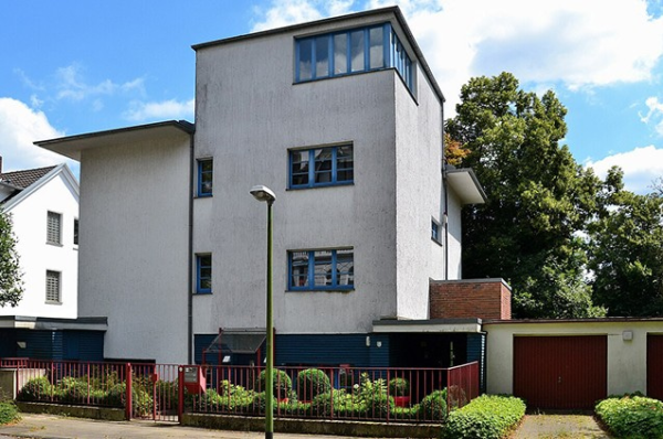 Mehrfamilienhaus mit heller Fassade, Garage und kleinem Vorgarten vor der Strasse.