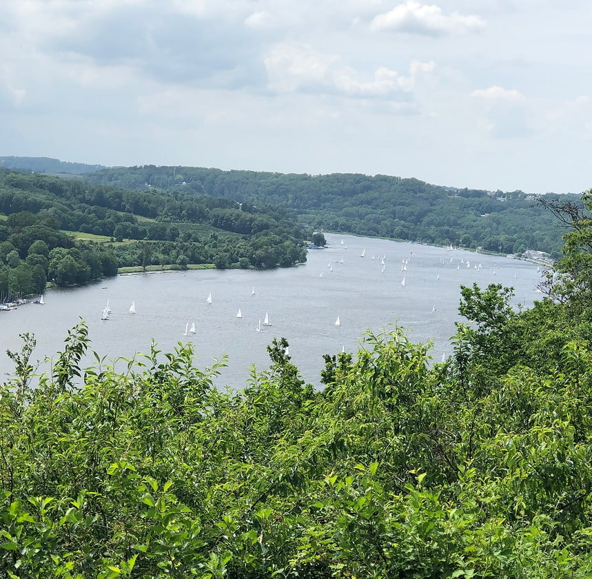 Blick über einen von Wald umgebenen See mit Segelbooten.