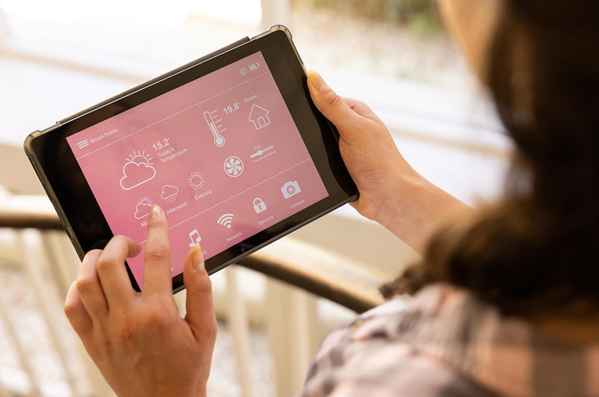 Frau steuert Heizung, Licht und Sicherheit ihrer Wohnung über eine Smart-Home-App auf dem Tablet.
