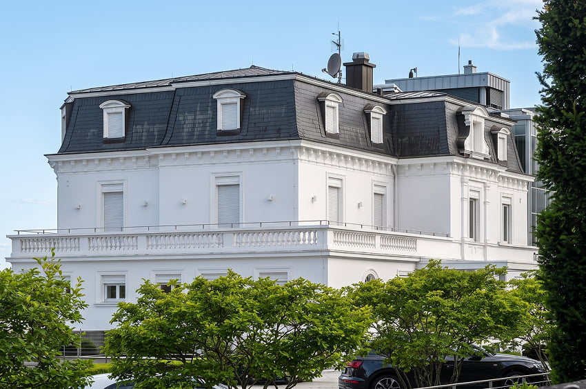 Repräsentative weiße Villa mit Mansarddach, Terrasse und begrüntem Grundstück.