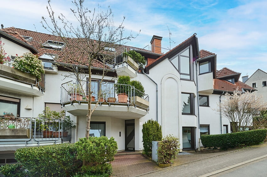 Wohnhaus mit Balkonen, gepflegtem Vorgarten und weißer Fassade.