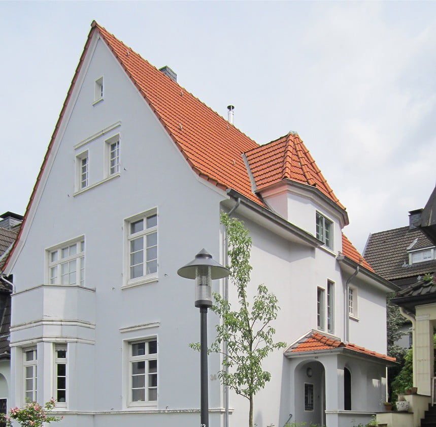 Helles Wohnhaus mit rotem Ziegeldach und klassischer Fassade.