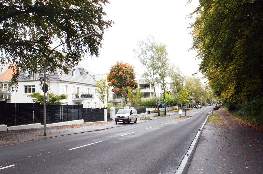 Baumgesäumte Wohnstraße mit Wohnhäusern, Gehweg und parkenden Fahrzeugen.