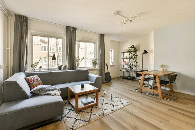 Helles Wohnzimmer mit grauem Sofa, Couchtisch, Teppich und Arbeitsplatz am Holztisch.